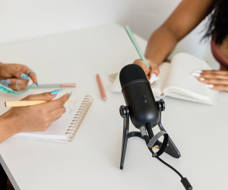 podcast microphone and two women writing on notepads