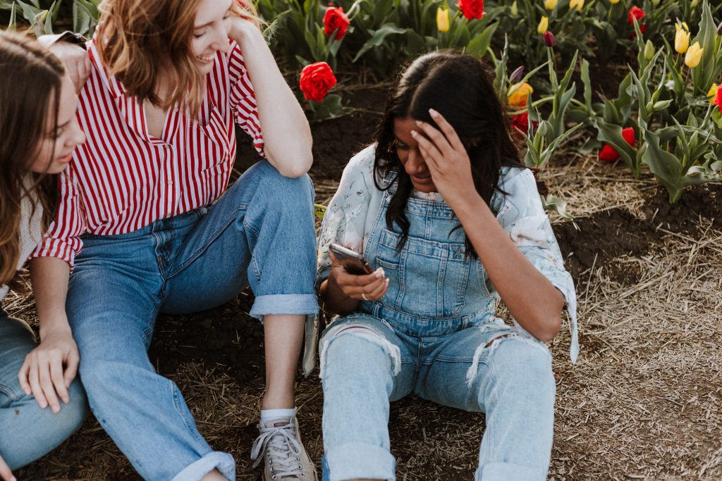 3 girls sitting on the ground, one looking at the phone in her hand