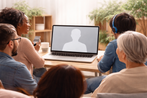 Diverse group of people attending an online community workshop on a laptop, engaging with a speaker on screen in a warm and collaborative environment, showing connection, empathy, and digital learning